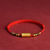 Close up of a red braided bracelet with a gold plated cylindrical bead
