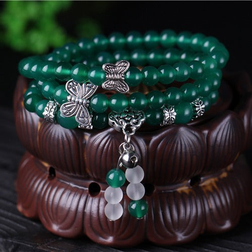 Multi-layer green agate bracelet with silver butterfly charms wrapped on a wooden stand