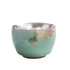 Close-up of a celadon tea cup showing the silver interior and butterfly motif
