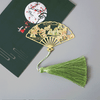 Gold-tone metal fan-shaped bookmark with green tassel resting on a book
