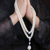 Hands holding a white bodhi seed mala necklace with a lotus pendant