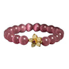 Close up of a pink cat's eye bead bracelet with a gold flower charm