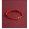A braided red cord bracelet with a small gold-tone ring charm on a dark red background