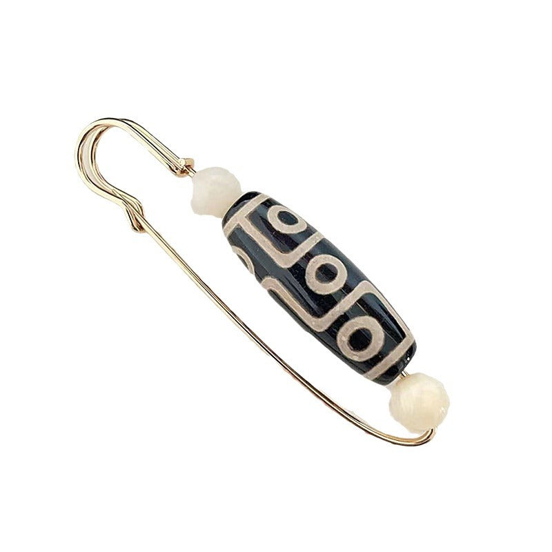 Gold-tone safety pin brooch with a black and white Nine-Eye Dzi bead center.