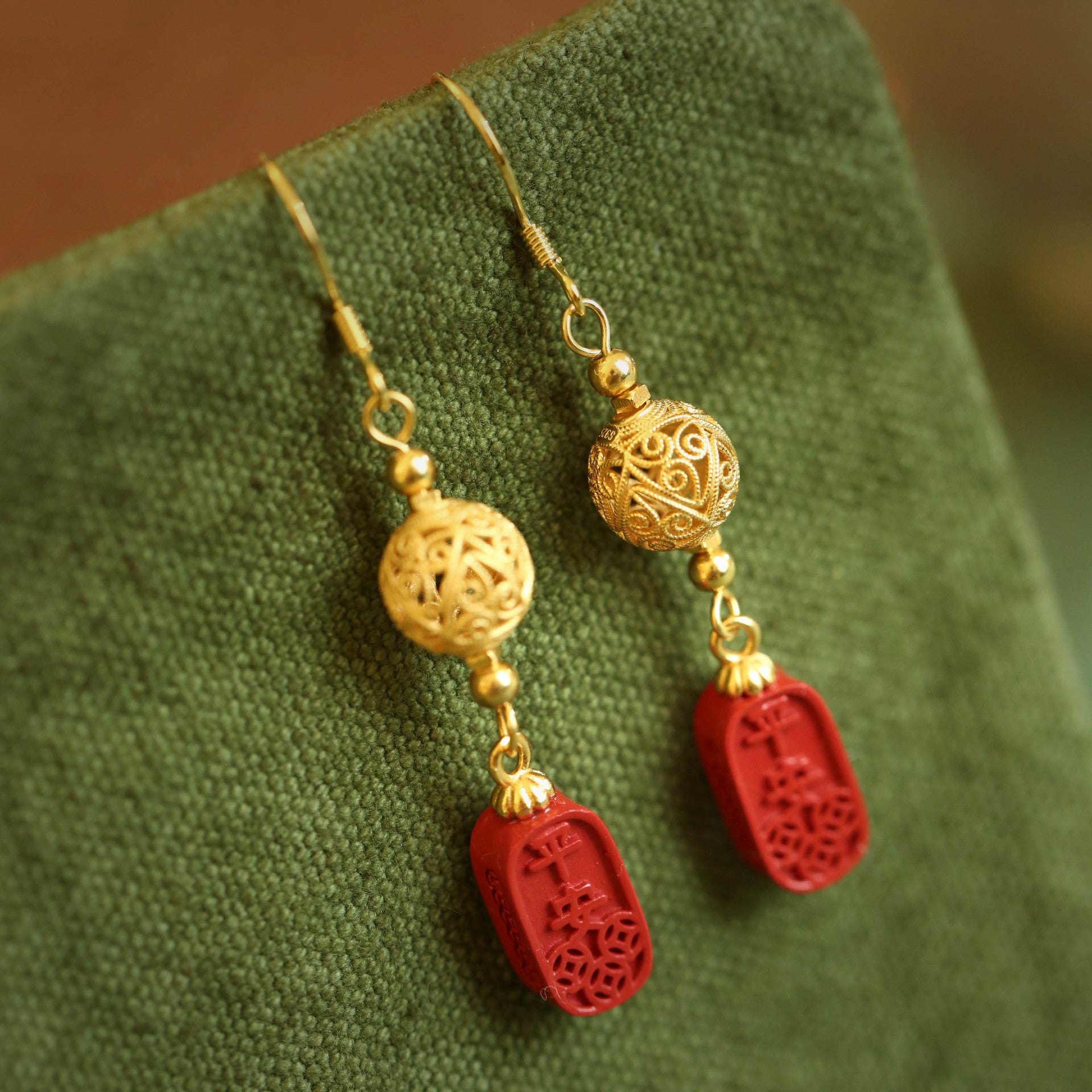 Gold tone copper earrings with red cinnabar gourd charms on a green background