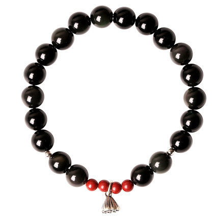 Black obsidian beaded bracelet with red cinnabar accents and a silver lotus pod charm resting on a ceramic stand.