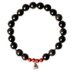 Black obsidian beaded bracelet with red cinnabar accents and a silver lotus pod charm resting on a ceramic stand.