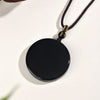 Close up of a smooth black round obsidian pendant on a dark braided cord