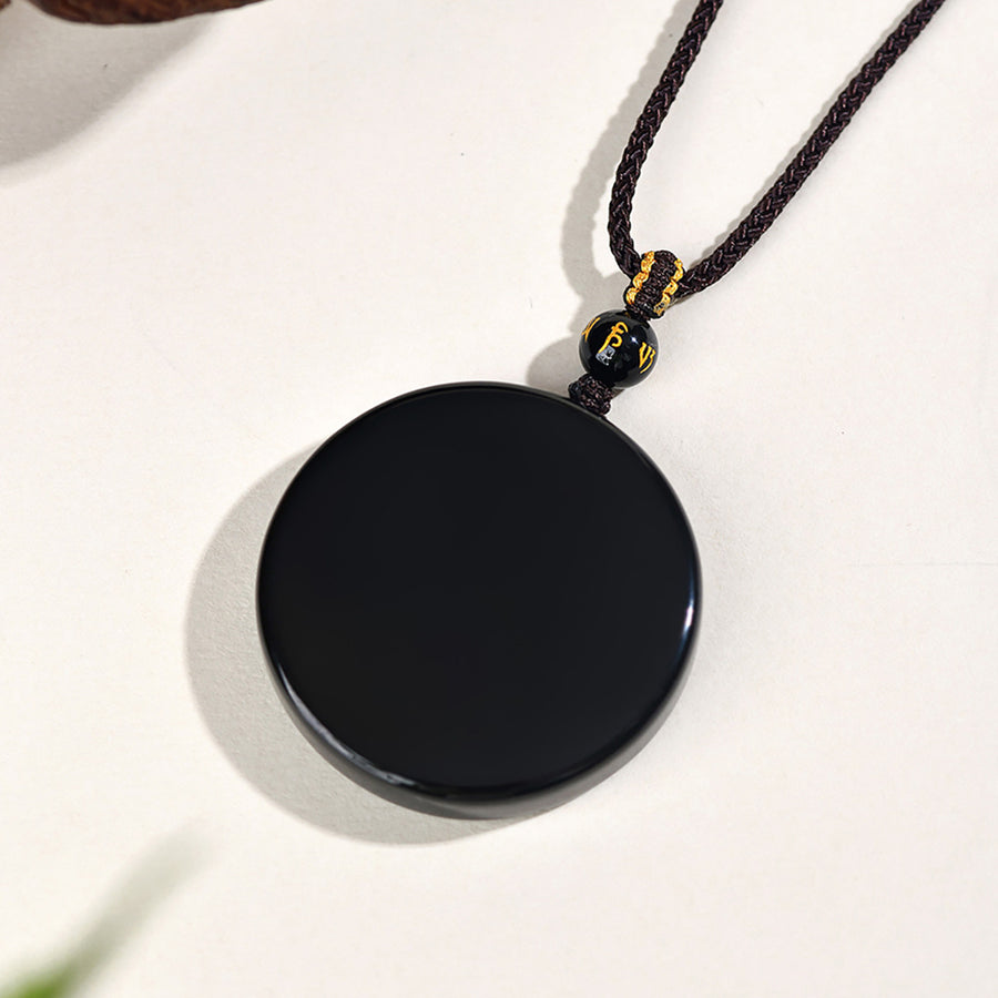 Close up of a smooth black round obsidian pendant on a dark braided cord