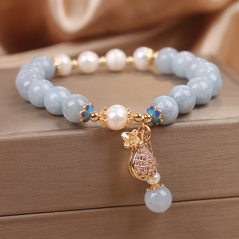 Close up of light blue crystal bracelet with pearl beads and gold money bag charm