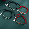 Black and red braided bracelets with a jade donut charm and silver tag on a green background