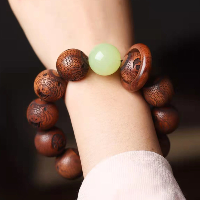 Close-up of a wooden bracelet with engraved tiger characters and a light green bead on a wrist.