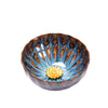 Hand holding a blue and brown ceramic teacup with a gold-tone lotus flower in the center