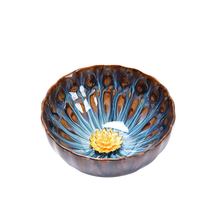 Hand holding a blue and brown ceramic teacup with a gold-tone lotus flower in the center