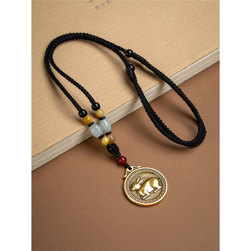 Close up of a brass Chinese zodiac pendant hanging from a black braided cord with accent beads