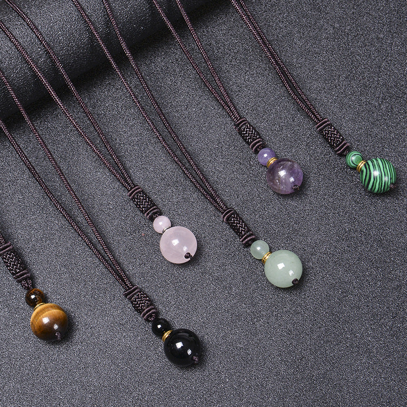 Six variations of a handmade natural stone pendant necklace on a dark cord laid out on a grey surface