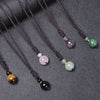Six variations of a handmade natural stone pendant necklace on a dark cord laid out on a grey surface