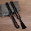 Long black beaded mala necklace with lava rock texture and tassel lying on wood