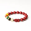 Red cinnabar beaded bracelet with a carved Pixiu charm and multi-colored accent beads on a gray surface