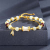 Close up of a gold tone bracelet with white glass beads and a central bamboo charm