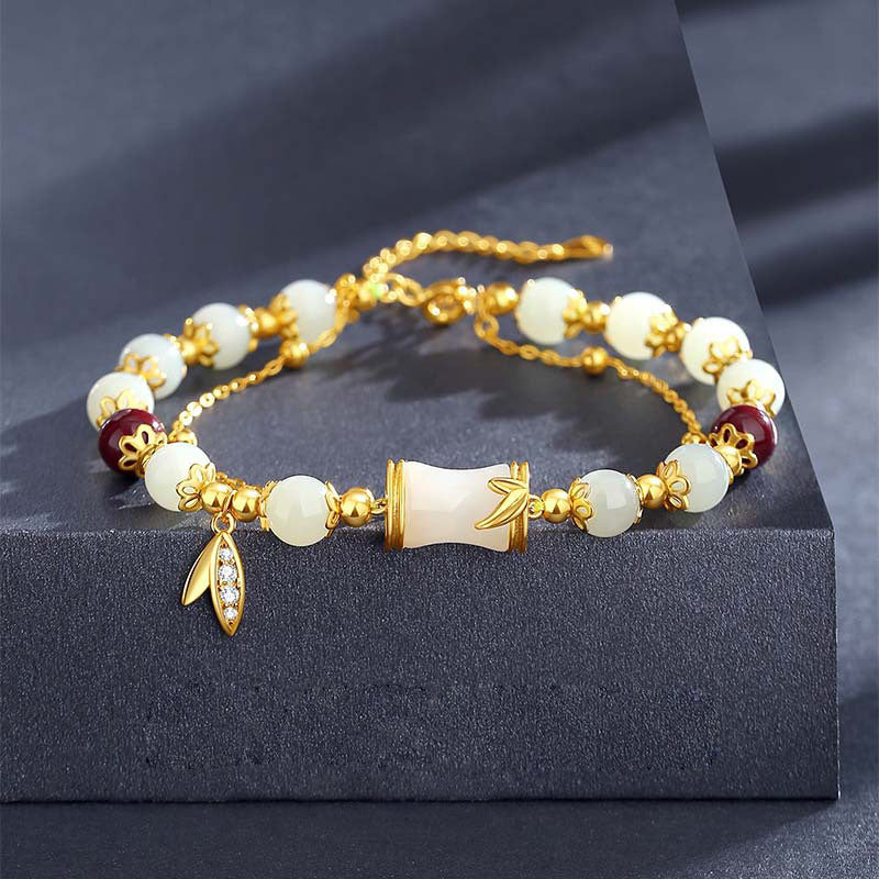 Close up of a gold tone bracelet with white glass beads and a central bamboo charm