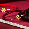 Close-up of a red braided string bracelet with a gold coin charm