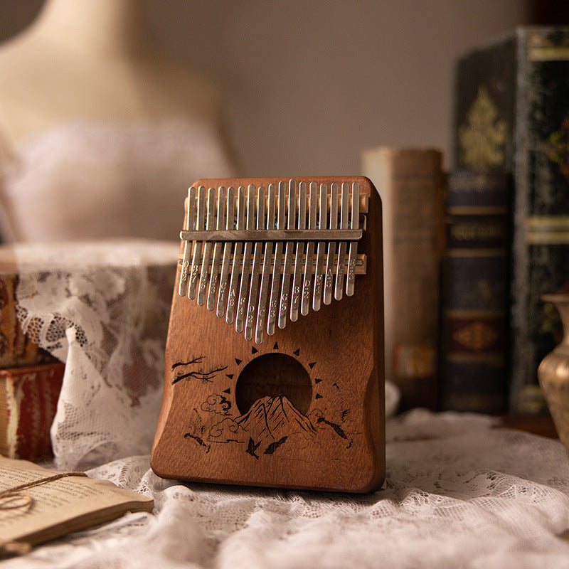 A wooden kalimba thumb piano with an engraved mountain design resting in a basket.