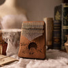 A wooden kalimba thumb piano with an engraved mountain design resting in a basket.