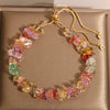 Close-up of a multi-colored crystal chip bracelet with a gold-tone adjustable chain on a beige background.
