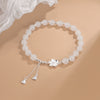 White beaded bracelet with silver flower charm and heart tassel on beige background