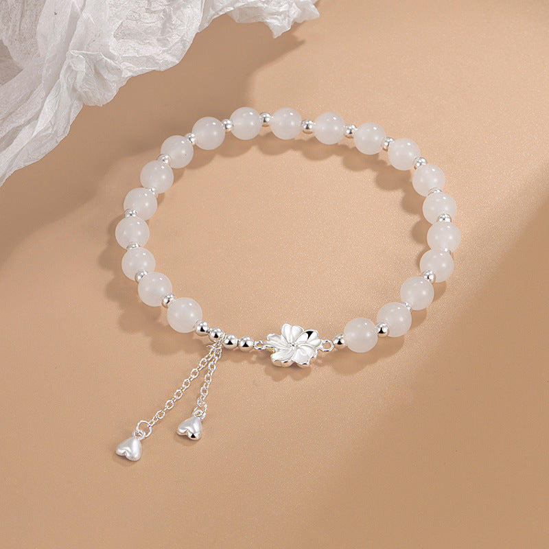 White beaded bracelet with silver flower charm and heart tassel on beige background