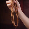 A hand holding a Star Moon Bodhi Seed Mala Necklace with a wooden pendant.