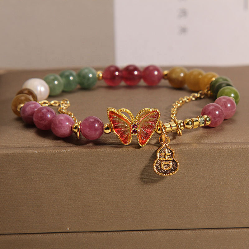Close-up of a colorful tourmaline beaded bracelet with a gold butterfly and gourd charm