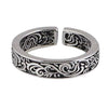 Close up view of a silver tone adjustable copper ring with black floral scrollwork pattern