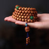Hand holding a coiled sandalwood mala bracelet with green beads