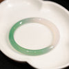 Close up of a smooth green and white gradient agate bangle bracelet on a white dish