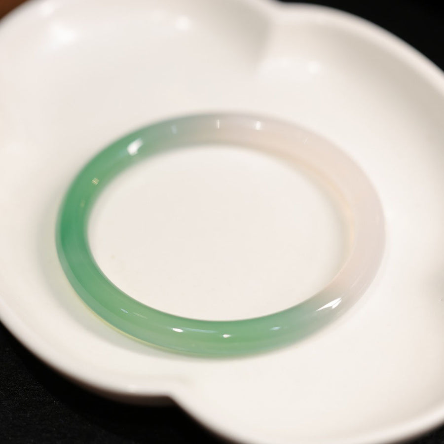 Close up of a smooth green and white gradient agate bangle bracelet on a white dish