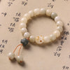 Close-up of a white bodhi seed bracelet with a cat paw charm and tassel on a paper background.
