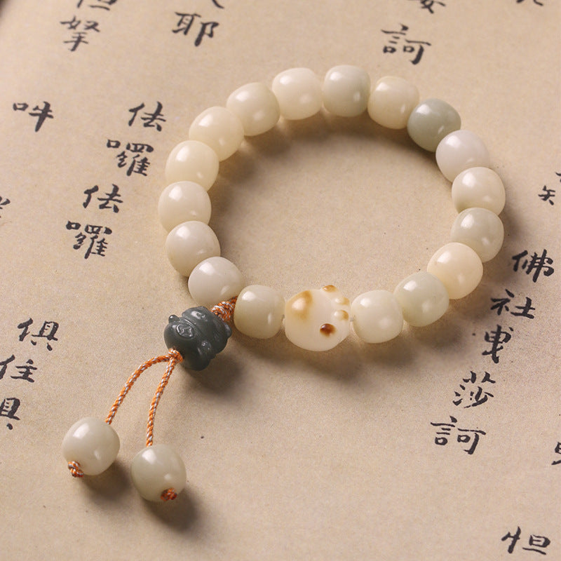 Close-up of a white bodhi seed bracelet with a cat paw charm and tassel on a paper background.