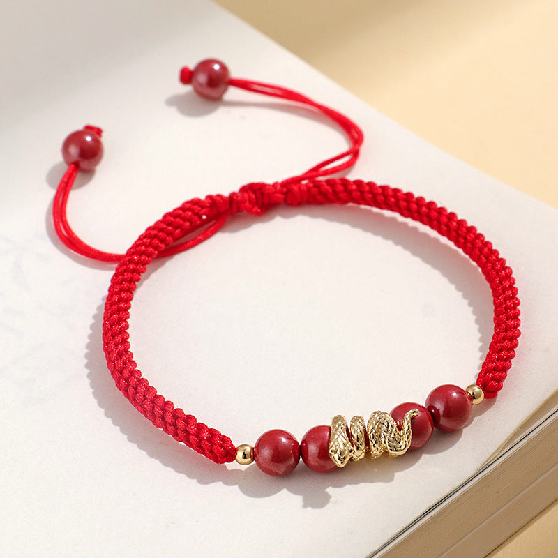 Close up of a red braided bracelet with a gold snake charm and red beads