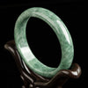 Natural deep bean green jade bangle bracelet on a wooden stand