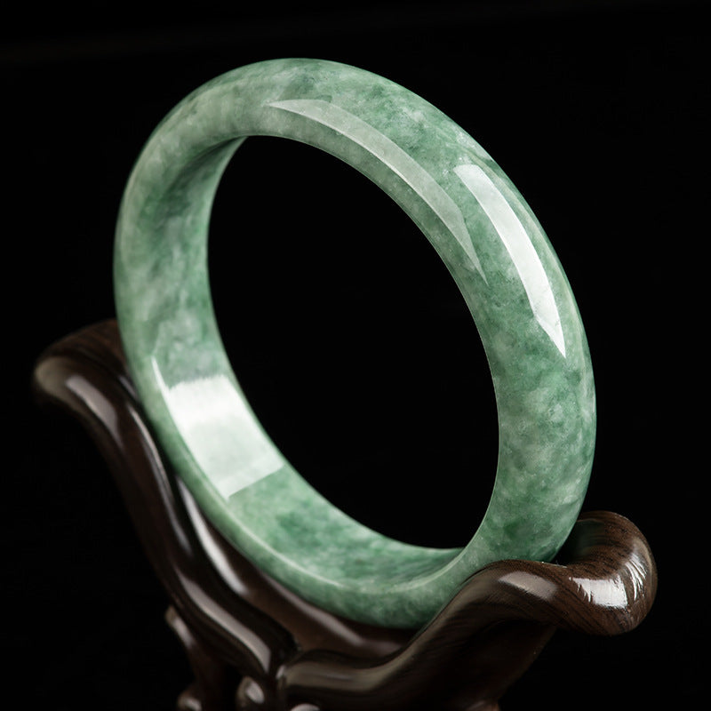 Natural deep bean green jade bangle bracelet on a wooden stand