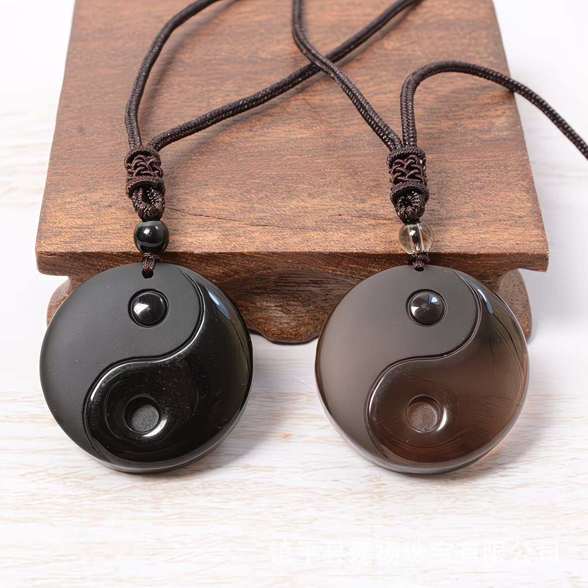 Two round black obsidian pendants with carved Yin Yang symbols on brown cords