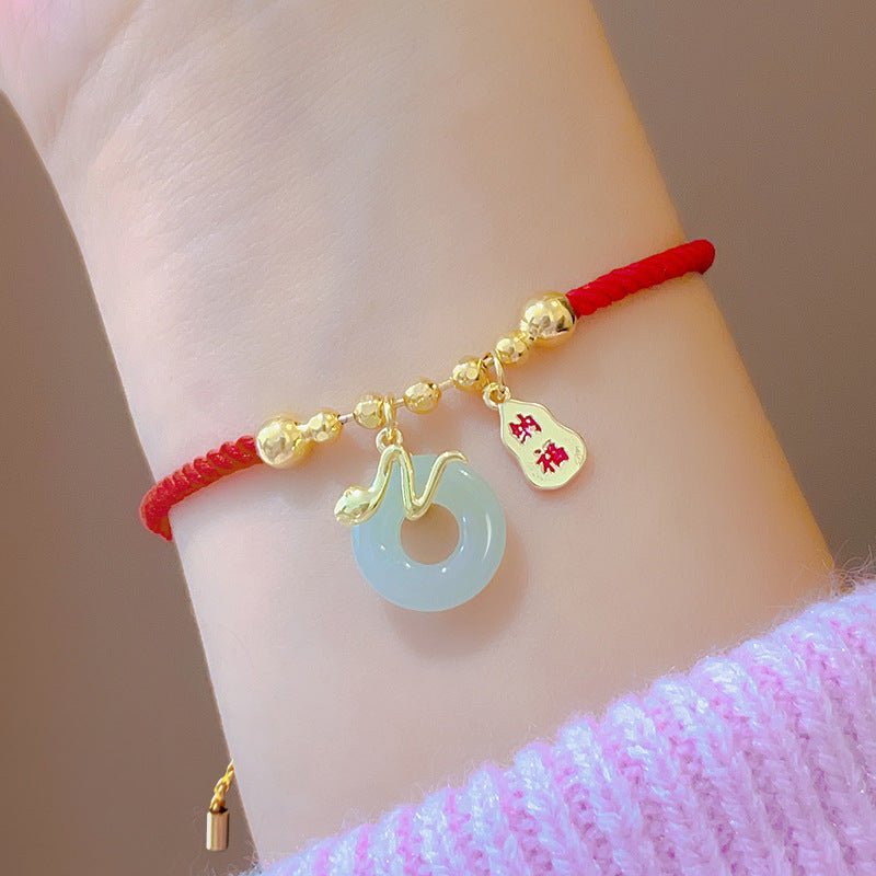 Gold snake charm and jade peace buckle on a red woven cord bracelet