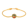 Close-up of a gold-tone copper snake chain bracelet with a red and green hexagonal charm featuring Buddhist script.
