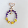 Close up of a beaded keychain with purple and yellow stones on a gold tone chain