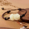 A close-up of a white jade Pixiu charm on a brown braided cord bracelet.