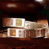 Hammered copper cuff bracelet with red and gold seal engravings on a wooden surface