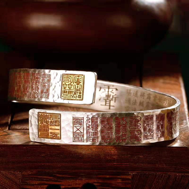 Hammered copper cuff bracelet with red and gold seal engravings on a wooden surface