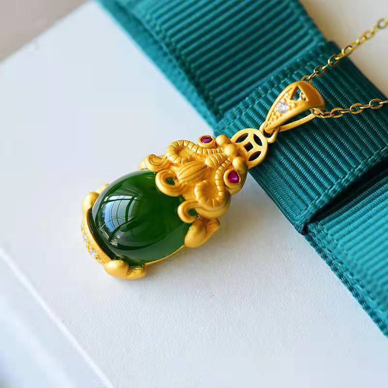 Close up of a gold-tone Pixiu pendant holding a smooth green jade stone